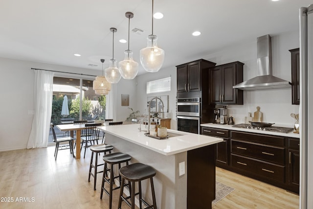 kitchen featuring visible vents, wall chimney range hood, a breakfast bar area, light countertops, and stainless steel appliances