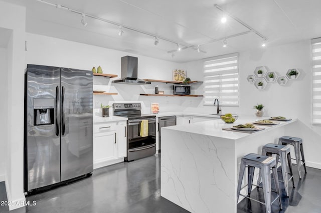 kitchen featuring wall chimney range hood, a breakfast bar, white cabinetry, stainless steel appliances, and kitchen peninsula