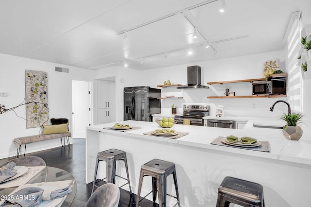 kitchen featuring a breakfast bar, sink, kitchen peninsula, stainless steel appliances, and wall chimney range hood