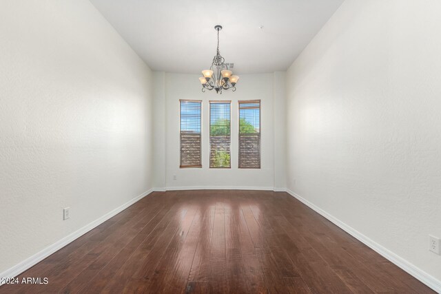 empty room featuring an inviting chandelier and dark wood-type flooring