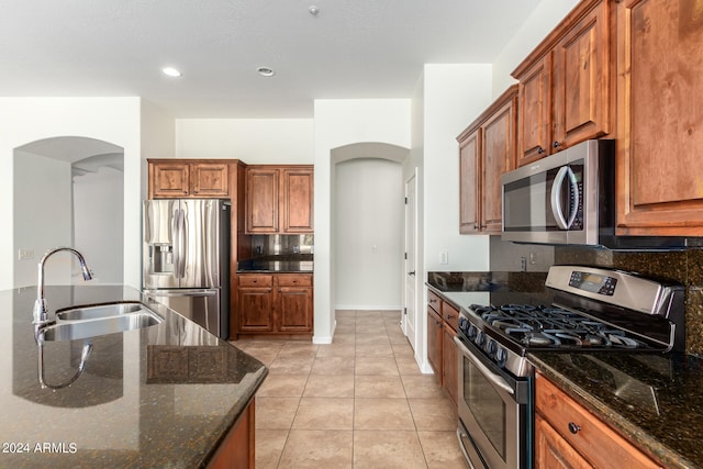 kitchen with dark stone countertops, light tile patterned floors, appliances with stainless steel finishes, and sink