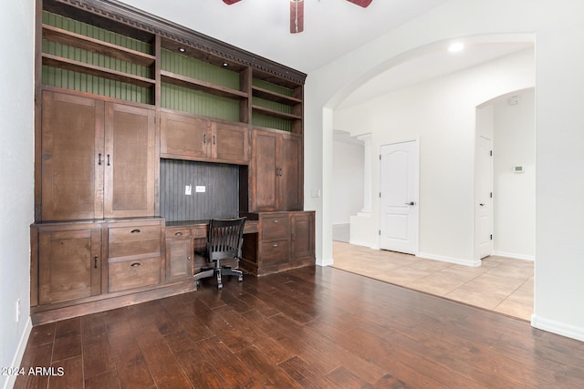 unfurnished office with built in desk, dark wood-type flooring, and ceiling fan