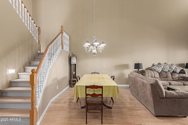 dining space with a chandelier, a high ceiling, baseboards, stairway, and light wood finished floors