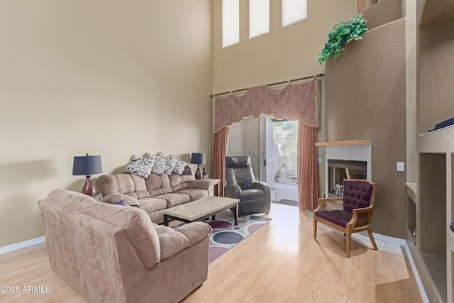 living area featuring light wood-style floors, a high ceiling, baseboards, and a tile fireplace