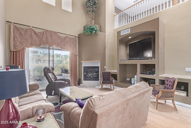 living room with built in features, visible vents, light wood-style flooring, a high ceiling, and a glass covered fireplace