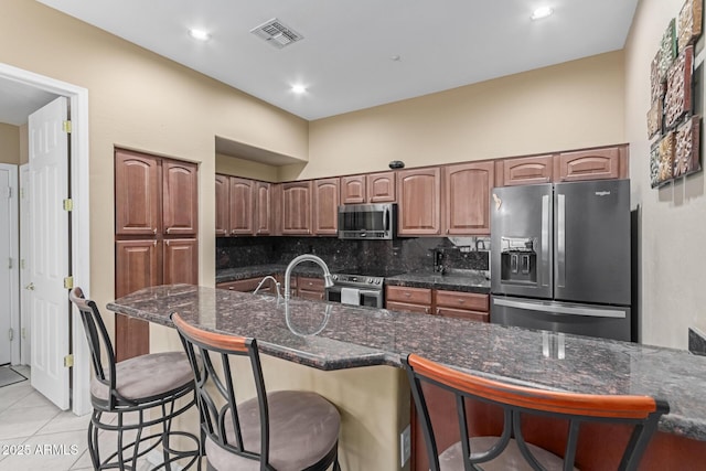 kitchen featuring light tile patterned floors, visible vents, decorative backsplash, appliances with stainless steel finishes, and a breakfast bar area