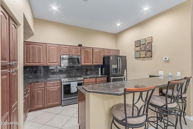 kitchen featuring brown cabinets, a breakfast bar area, light tile patterned floors, stainless steel appliances, and decorative backsplash