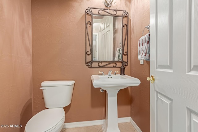 bathroom featuring toilet, tile patterned flooring, baseboards, and a textured wall