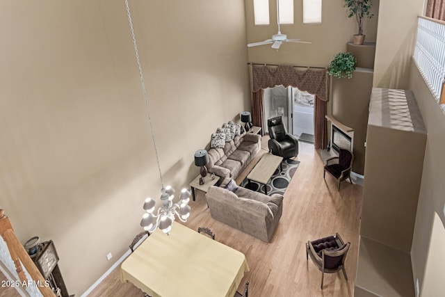 living room with a fireplace, baseboards, wood finished floors, and ceiling fan with notable chandelier