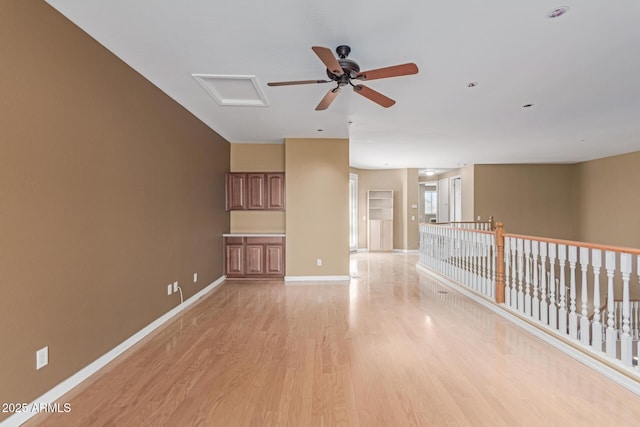 empty room with attic access, light wood-type flooring, and baseboards