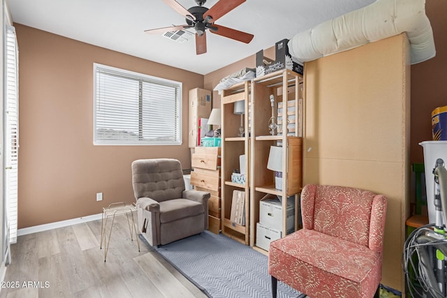 living area featuring a ceiling fan, visible vents, baseboards, and wood finished floors