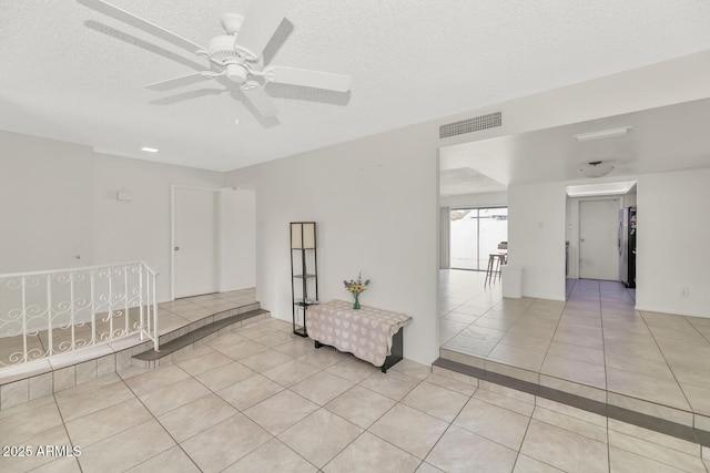 tiled empty room with ceiling fan and a textured ceiling