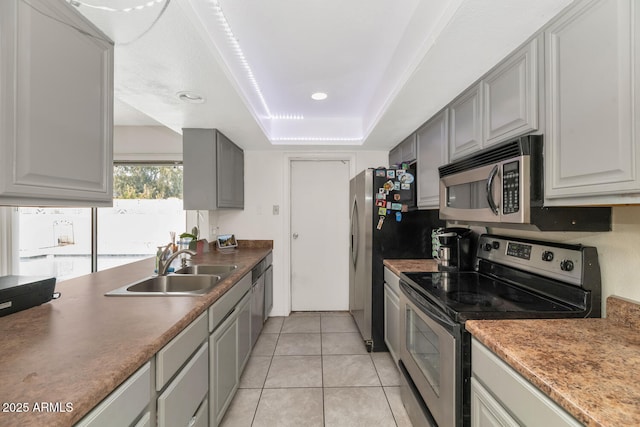 kitchen with light tile patterned flooring, sink, appliances with stainless steel finishes, gray cabinets, and a raised ceiling