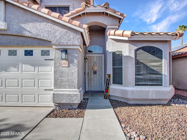 entrance to property with a tiled roof, an attached garage, and stucco siding