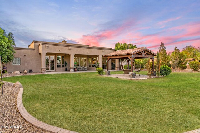 6861 W Calle Lejos, Peoria, AZ 85383 - back of property at dusk featuring a gazebo, stucco siding, a lawn, and a patio area