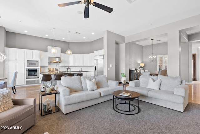 living room with ceiling fan with notable chandelier, light colored carpet, and sink