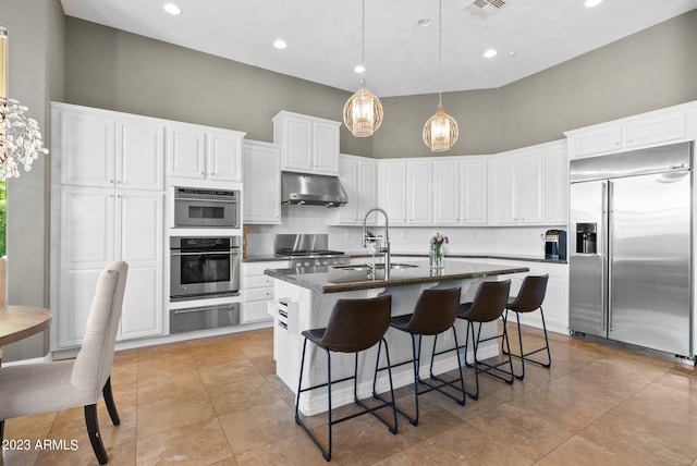 kitchen with a kitchen island with sink, sink, stainless steel appliances, exhaust hood, and a high ceiling