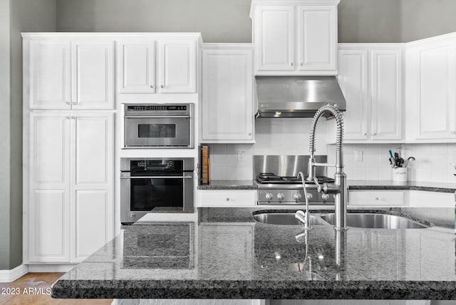 kitchen featuring a kitchen island with sink, wall chimney exhaust hood, white cabinetry, dark stone countertops, and decorative backsplash