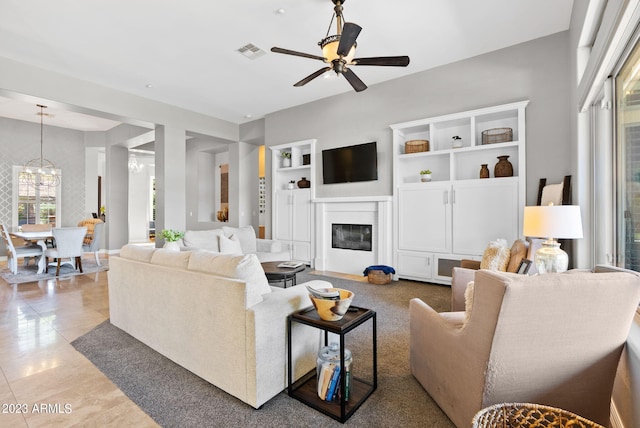 living room featuring ceiling fan with notable chandelier, built in shelves, and light tile patterned floors