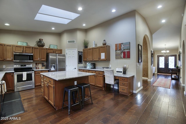 kitchen featuring brown cabinets, visible vents, appliances with stainless steel finishes, and high vaulted ceiling