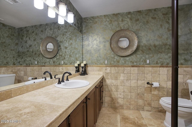 bathroom with toilet, tile walls, wainscoting, and vanity