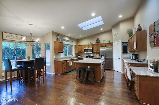 kitchen featuring brown cabinetry, visible vents, a chandelier, a kitchen island, and appliances with stainless steel finishes