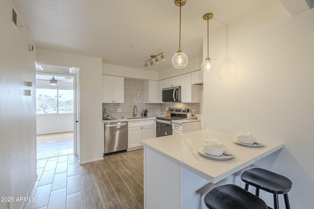 kitchen with a sink, tasteful backsplash, appliances with stainless steel finishes, a peninsula, and light wood finished floors