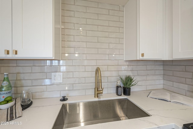 kitchen featuring white cabinetry, light stone countertops, tasteful backsplash, and a sink