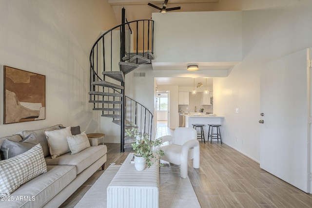 living area featuring stairway, a ceiling fan, visible vents, light wood-style flooring, and a high ceiling