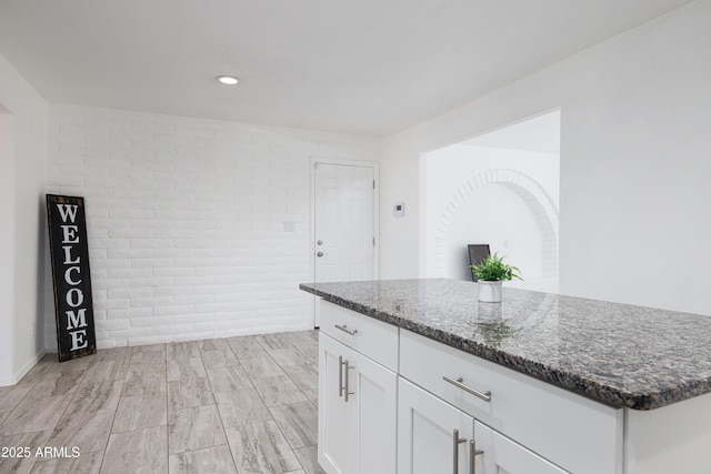 kitchen featuring recessed lighting, brick wall, white cabinetry, dark stone counters, and light wood-type flooring