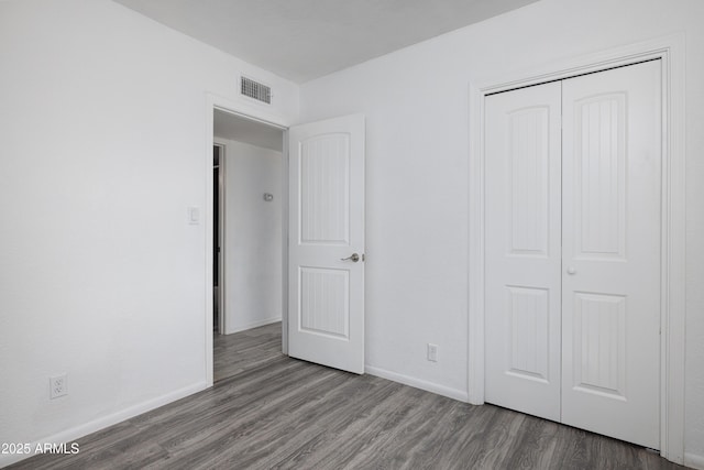 unfurnished bedroom featuring baseboards, a closet, visible vents, and wood finished floors