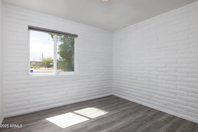 spare room with brick wall, baseboards, and dark wood finished floors