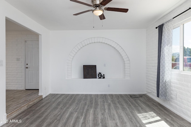 unfurnished living room with a ceiling fan, brick wall, plenty of natural light, and wood finished floors