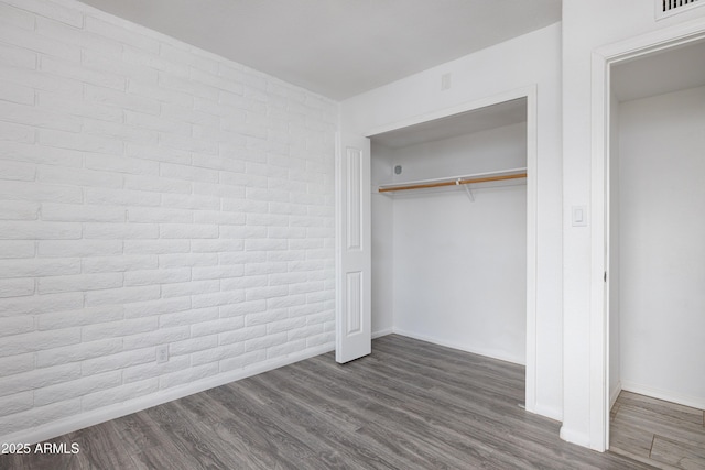 unfurnished bedroom with baseboards, dark wood-style flooring, a closet, and brick wall