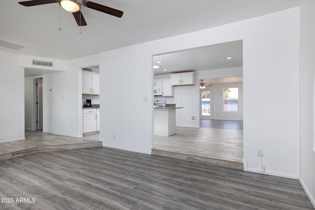 unfurnished living room featuring baseboards, visible vents, ceiling fan, and wood finished floors
