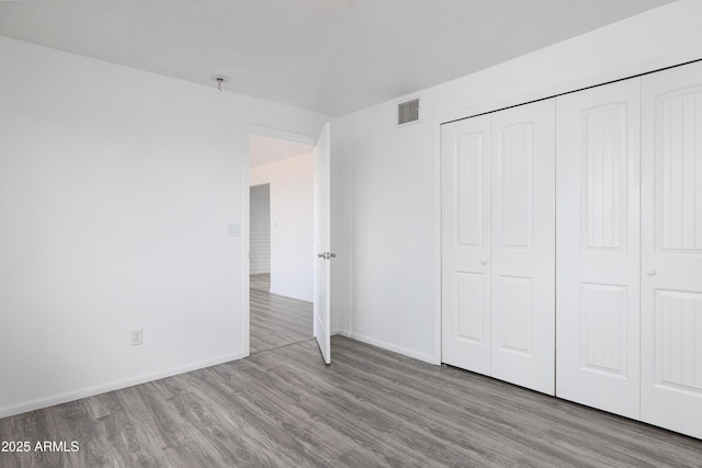 unfurnished bedroom featuring a closet, visible vents, wood finished floors, and baseboards