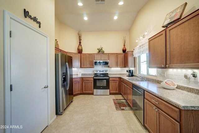 kitchen featuring appliances with stainless steel finishes, tasteful backsplash, vaulted ceiling, sink, and light tile patterned floors