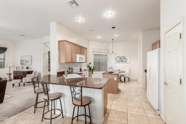 kitchen with light tile patterned floors, white appliances, visible vents, a kitchen island, and a sink