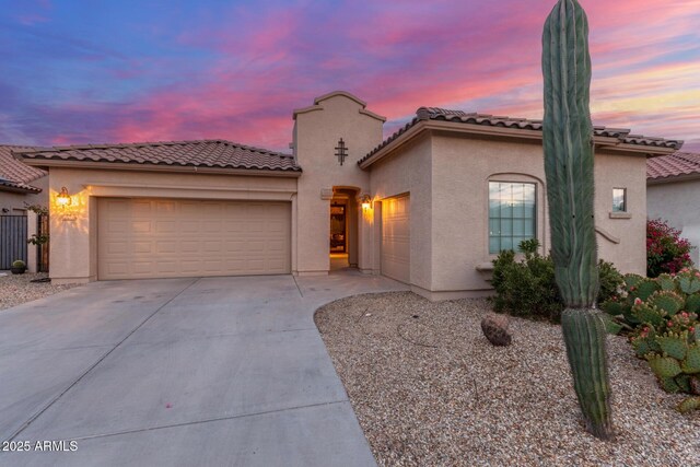 mediterranean / spanish-style home with an attached garage, a tiled roof, driveway, and stucco siding