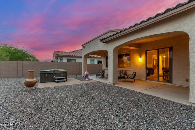 rear view of house with stucco siding, a patio area, a fenced backyard, and a hot tub