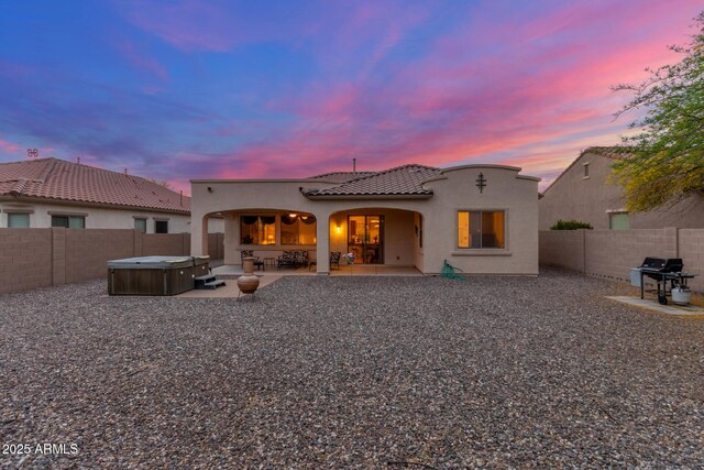 back of house at dusk with a hot tub, a fenced backyard, stucco siding, a patio, and a tile roof