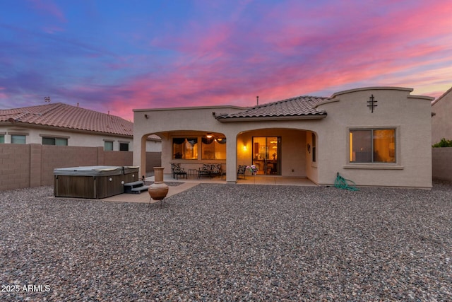 back of property with a hot tub, a tiled roof, fence, a patio, and stucco siding