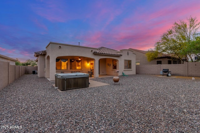 back of property featuring stucco siding, a tile roof, a fenced backyard, and a hot tub