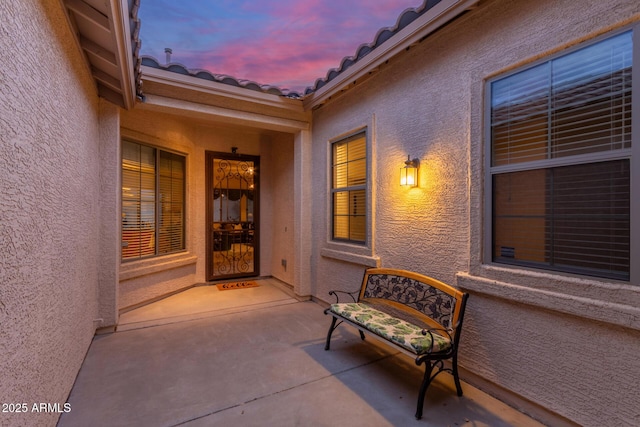 view of exterior entry featuring a tiled roof, a patio area, and stucco siding
