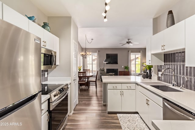 kitchen featuring ceiling fan with notable chandelier, a peninsula, a sink, stainless steel appliances, and open floor plan