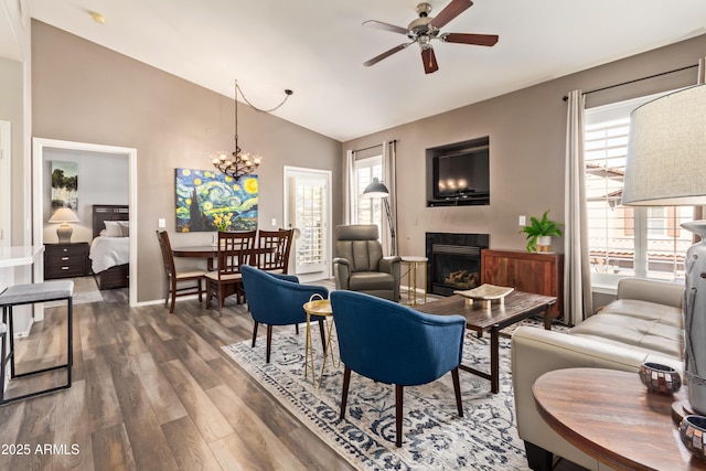 living area featuring a healthy amount of sunlight, ceiling fan with notable chandelier, a fireplace, and vaulted ceiling