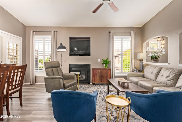 living area with light wood-style flooring, a healthy amount of sunlight, a ceiling fan, and a glass covered fireplace