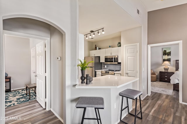 kitchen with visible vents, appliances with stainless steel finishes, dark wood-style flooring, light countertops, and a breakfast bar area