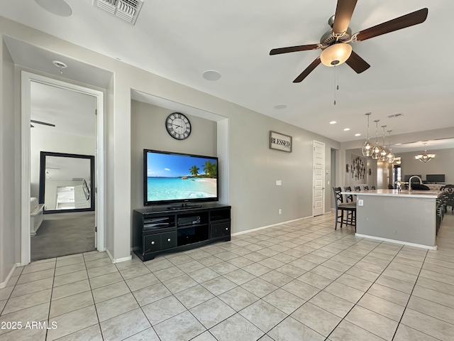 unfurnished living room with visible vents, baseboards, light tile patterned floors, ceiling fan with notable chandelier, and a sink