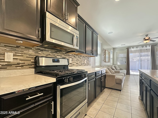 kitchen featuring open floor plan, decorative backsplash, appliances with stainless steel finishes, light tile patterned flooring, and a ceiling fan